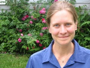 A photograph of Kate wearing a blue shirt and standing in front of flowers